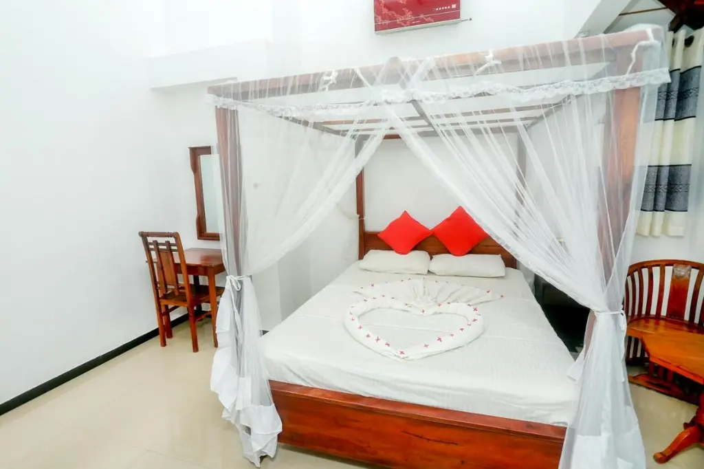 Double room with a four-poster bed, white mosquito-net canopy and red cushions