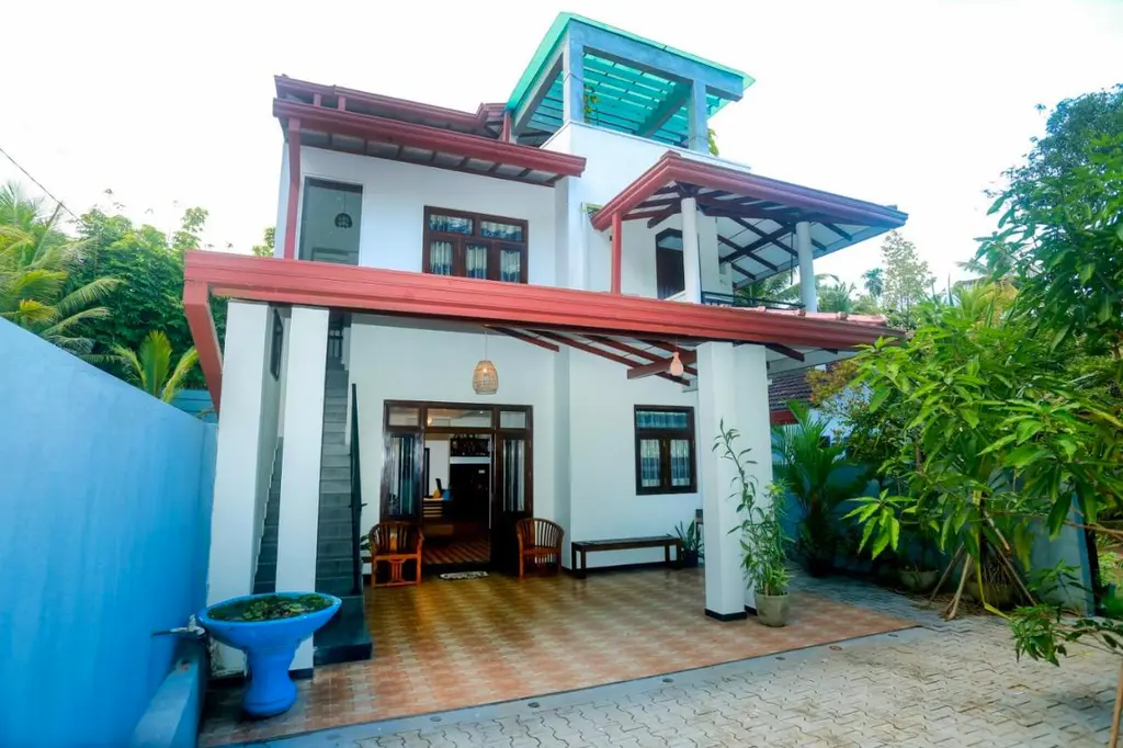Front of Jeju Villa & Apartment: a two-storey white house with red trims and a tiled forecourt