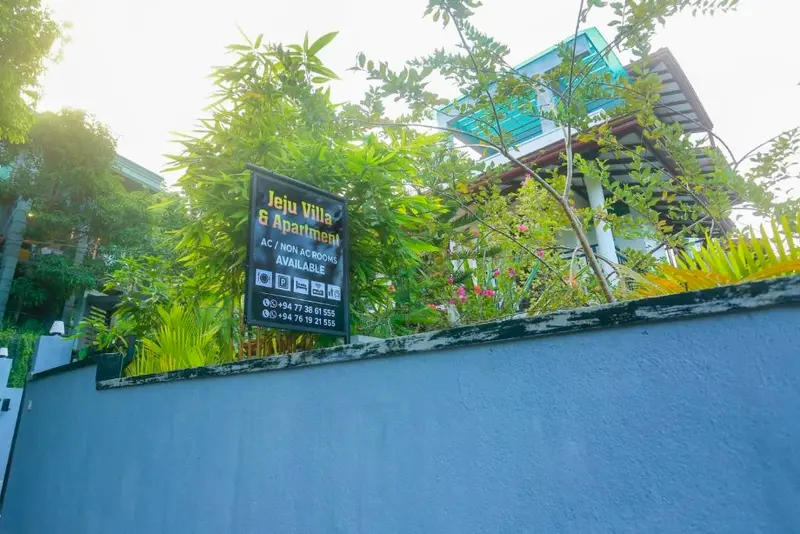 The Jeju Villa & Apartment sign on the garden wall, framed by bamboo and bougainvillaea