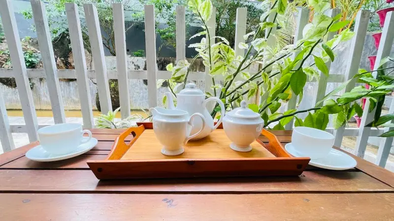 White tea set on a teak tray on the veranda, with garden greenery behind